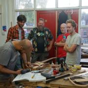 Guitar nearing completion surrounded by some of the volunteers who worked on it with Gavin  Pond at Pi Guitars,